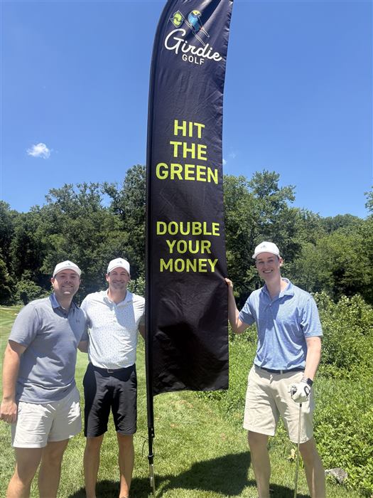 Three golfers beside the Girdie Golf banner